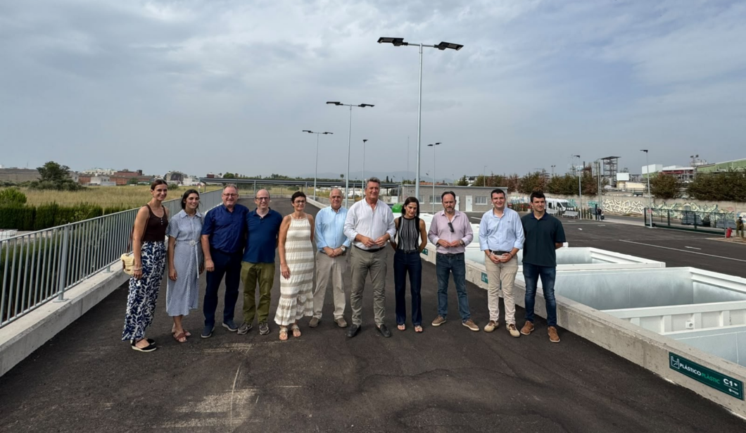 Group of diverse adults posing for a photo on a rooftop parking area with an industrial backdrop and open sky behind them.