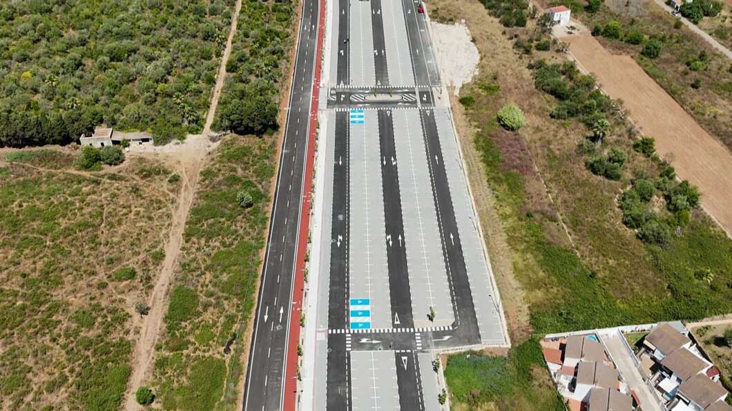 Aerial view of a newly built divided highway with an overpass, surrounded by fields and scattered houses in a rural area.