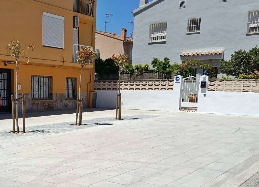 Quiet residential plaza with tiled paving, orange building on the left and a pale blue-gray building with a gate on the right.