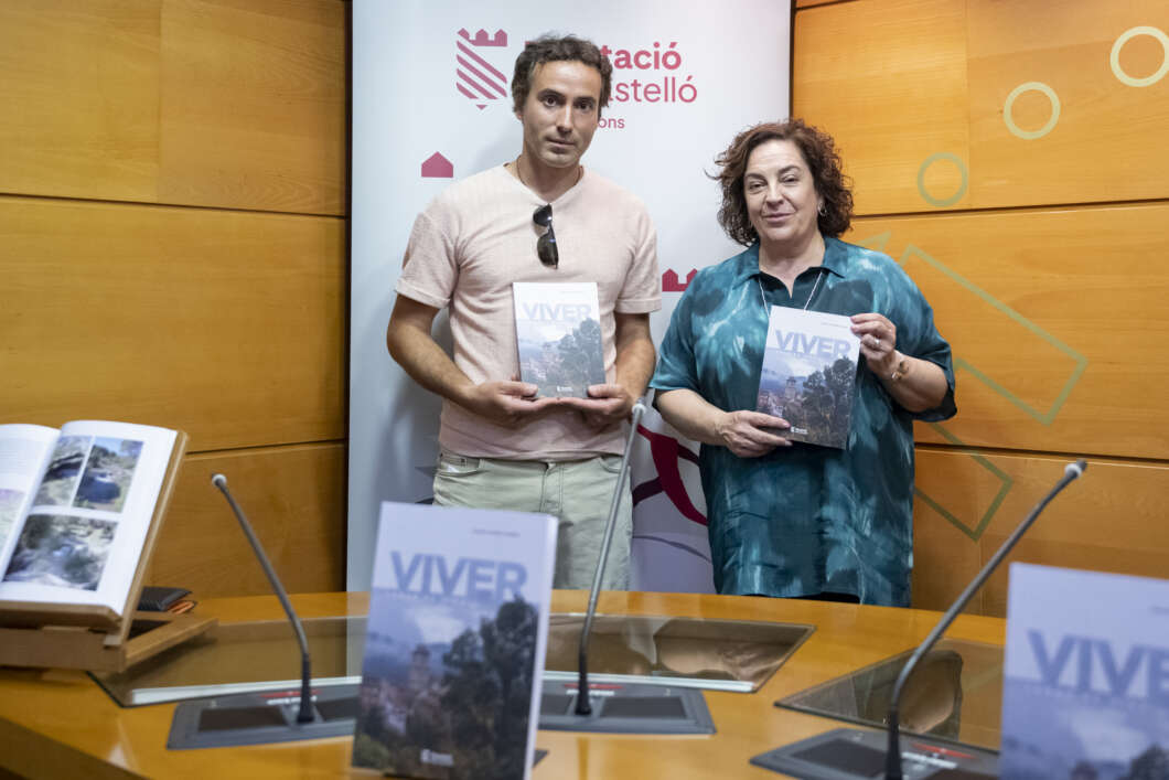 Two adults stand in a wood-paneled room, each holding a copy of the book titled VIVER at a book launch event.
