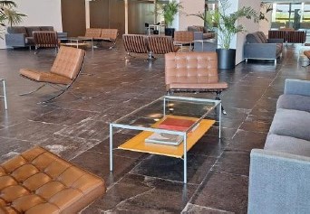 Modern lounge area in a spacious lobby with brown leather chairs, gray sofas, and a glass coffee table with magazines.