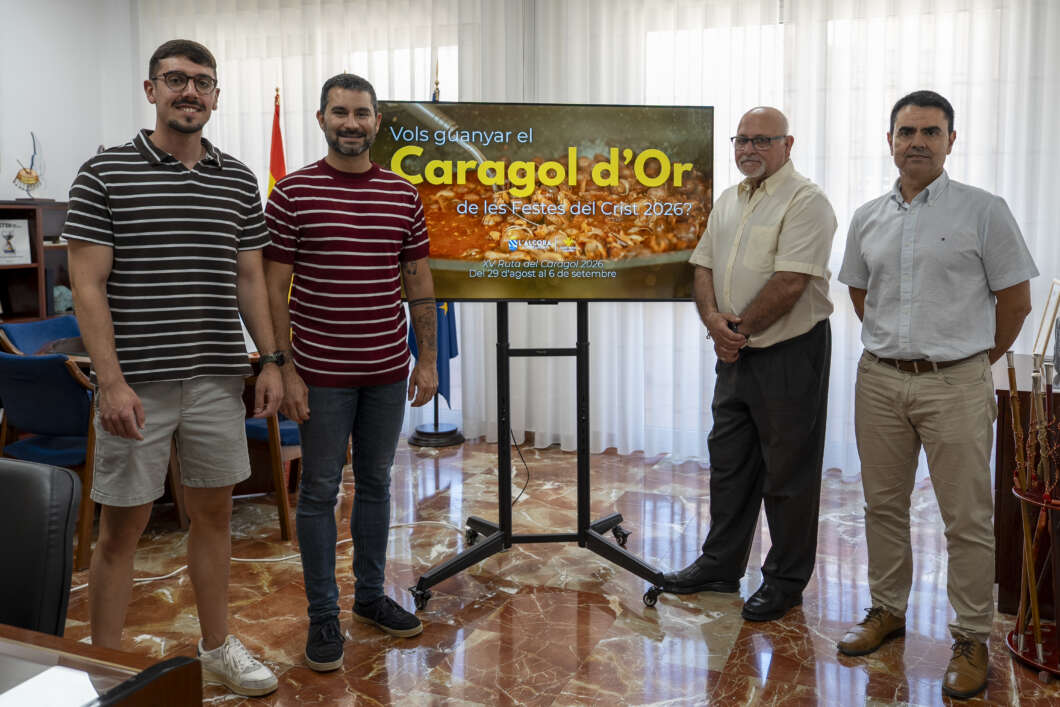 Four men stand in a room beside a large screen displaying 'Caragol d'Or' promo text for a Crist 2026 event.
