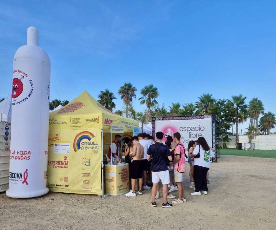Group of people at an outdoor health/awareness fair, standing in line at a yellow information tent beside a tall white inflatable bottle.