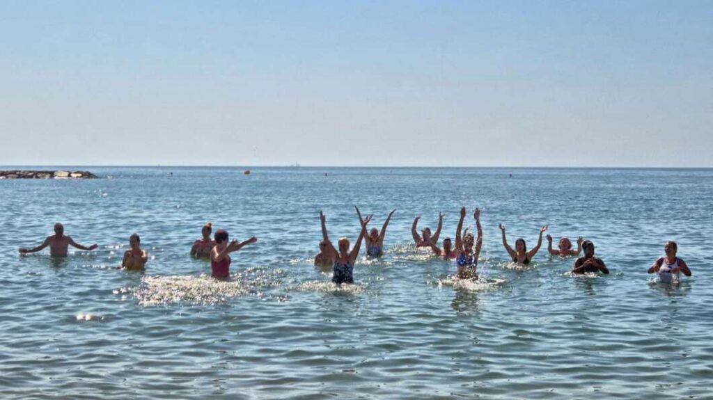 Group of people swimming and splashing in the shallow ocean water on a sunny day, near the shore.