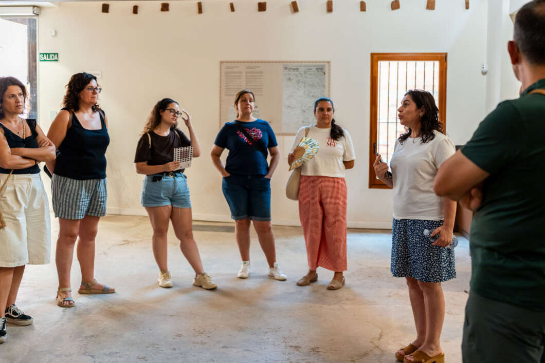 Instructor woman speaking to a circle of seven adults in a bright workshop space.