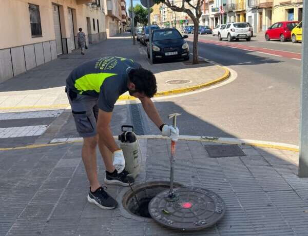 Civic worker in a neon vest opens a street manhole using a power tool on a city sidewalk.